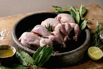 Raw uncooked quails ready for marinat in clay tray with lime, salt, pepper and greens over wooden table. - obrazy, fototapety, plakaty