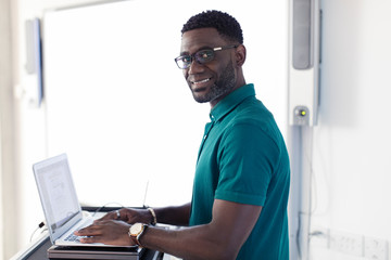 Portrait smiling confident male instructor at laptop in classroom