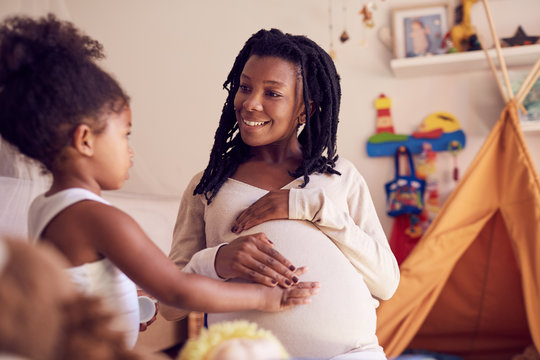 Cute toddler daughter touching mother‚Äôs pregnant belly