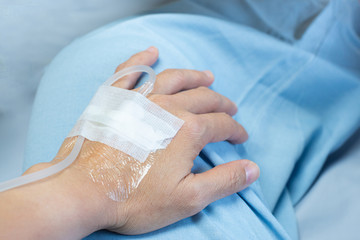 Hand of patient lying on bed in ward at hospital with saline solution tube injection and sterile plaster bandage on hand.