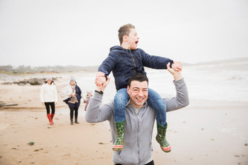 Happy father carrying son with Down Syndrome on shoulders on beach