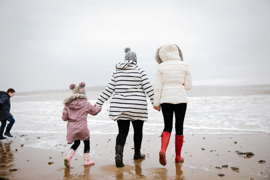 Family in warm clothing walking on winter ocean beach