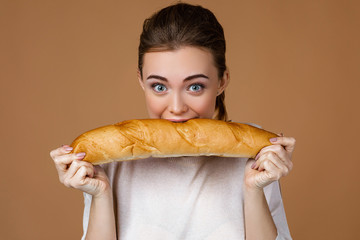 Portrait of beautiful young woman eating delicious bread baguette on studio yellow background. girl...
