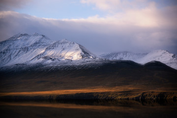 Beautiful snow mountain in Husavik, Iceland with warm light of sunset, beautiful cloud and sky as well as reflection of water and mountain. Idea for  any backgrounds used.
