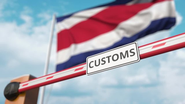 Barrier gate with CUSTOMS sign being closed with flag of Costa Rica as a background. Costa Rican border closure or protective tariffs