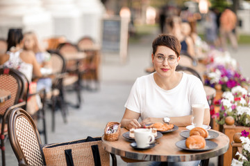 A woman dines in a street cafe. Lesbian woman with short male haircut eats croissants for Breakfast in a restaurant on the street