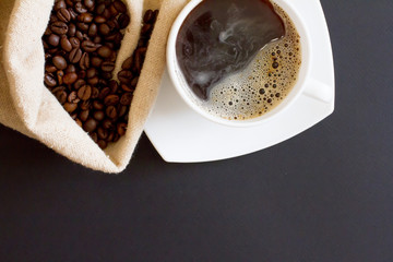 coffee beans in a bag with a white Cup of fresh coffee on a black background. space for text, top view.