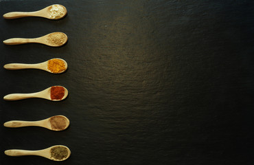 Photography of powder spices in little wooden spoons on a slate for food background