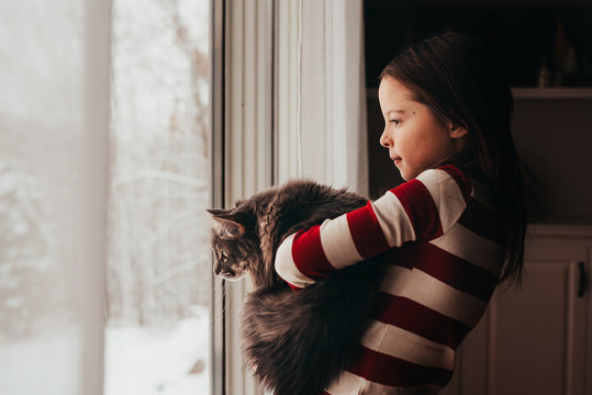 Girl standing by a window cuddling her cat