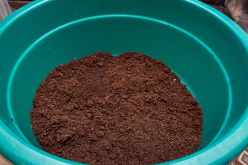 A plastic box round basin filled with black soil prepared for planting seeds of plants of seedlings of flowers and vegetables on a wooden table in the house.