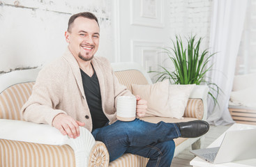 Handsome smiling man with cup of coffee sitting on couch at home