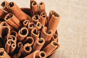 Obraz na płótnie Canvas Closeup detail - Heap of cinnamon bark sticks in wooden cup on linen tablecloth.