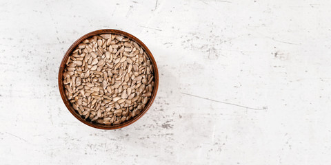 Sunflower seeds in small wooden bowl laying on white stone board, view from above, wide photo with...