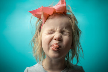 girl is mischievous. rebellious child. little girl with a pink bow on a blue background. girl shows...