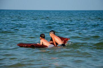 Friends on a water mattress float on the sea.