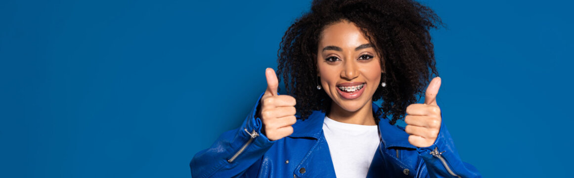 smiling african american woman showing thumbs up on blue background, panoramic shot