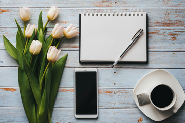 White bouquet of tulips on wooden background with coffee Cup, smartphone and empty notebook