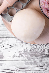 Dough, meat mince, lattice and rolling pin on the white wooden table. Ingredients and utensils to cook dumplings
