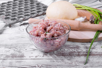 Dough, meat mince, lattice and rolling pin on the white wooden table. Ingredients and utensils to...