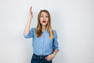 young blond positive woman looks excited raising her hand to ask question standing on isolated white background