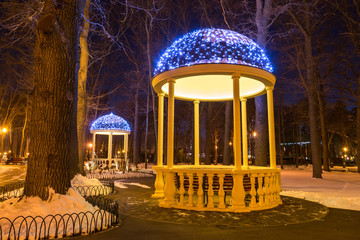Two arbors with electric garlands in city park at winter