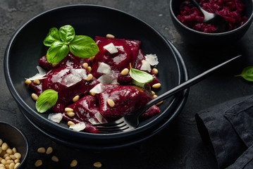 Beetroot ravioli with goat cheese, pine nuts and basil in a black plate on a black background....
