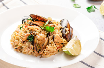 Seafood risotto in a white plate on the served table. Risotto with shrimp, tomatoes, parsley and mussels in shells. Tasty and healthy Mediterranean cuisine.