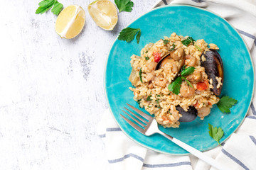 Seafood risotto in a blue plate on a gray background, top view, copy space. Risotto with shrimp, tomatoes, parsley and mussels in shells. Tasty and healthy Mediterranean cuisine. Free space for text.