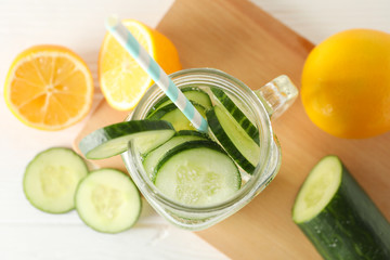 Glass jar with cucumber water on wood board, top view