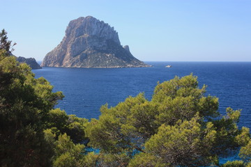 The solitary islet of Es Vedra in contrast against the blue sea of ​​Ibiza immersed in the...