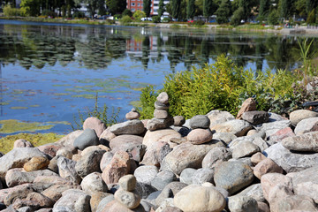 Fototapeta na wymiar Stacks of natural rocks by the beach of lake Valkeinen in Kuopio, Finland. Beautiful inspiring zen like view to a garden with rocks by the water. Relaxing, simple view, perfectly peaceful and idyllic.