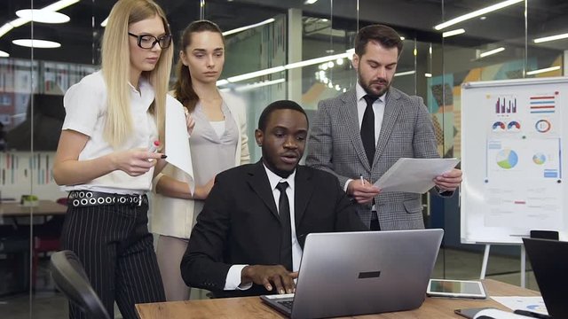 Front view of the clever experienced african american businessman which showing to his considerate purposeful male and female business colleagues the computer business plan