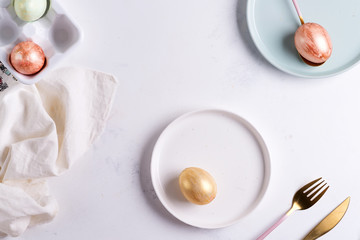 Easter table setting from above. Elegant empty plate, cutlery, napkin and golden eggs on stone
