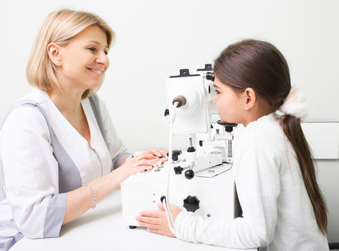 Mixed race girl is being examined at ophthalmic clinic. Female doctor using synoptophore doing eye diagnosis. Strabismus treatment