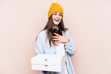 Young caucasian woman holding pizzas isolated laughs out loudly keeping hand on chest.