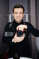 Photographer in black clothes taking a selfie with the camera in the mirror and smiling