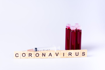Coronavirus letters sign with small test tube with blood and needle injection on white background 