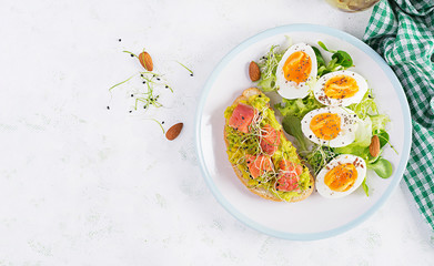 Breakfast. Healthy open sandwich on  toast with avocado and salmon, boiled eggs, herbs, chia seeds on white plate  with copy space. Healthy protein food. Top view, overhead