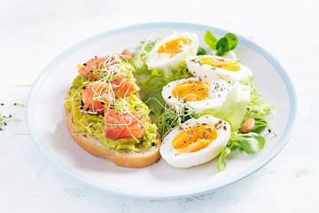 Breakfast. Healthy open sandwich on  toast with avocado and salmon, boiled eggs, herbs, chia seeds on white plate  with copy space. Healthy protein food.