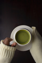 Female hands holding a white mug of matcha green tea