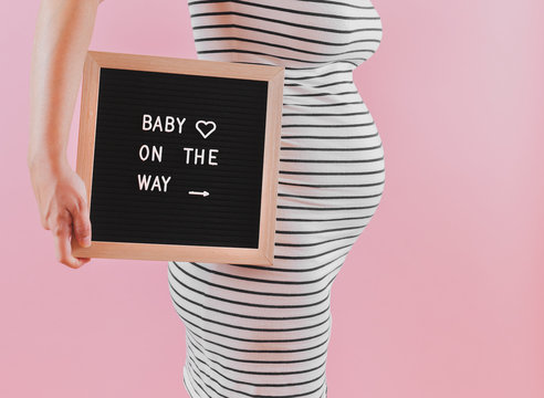 Pregnant Woman Announcing Her Pregnancy Using A Letterboard That Says 