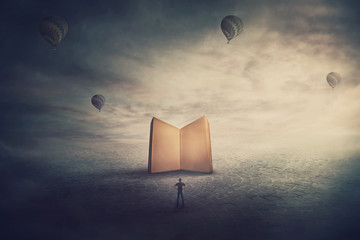 Surreal scene, imaginary world, tiny man stands in front of a giant opened book with empty blank...