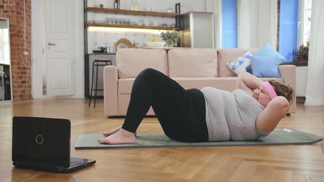 Young obese woman doing abs crunch exercise on floor at home