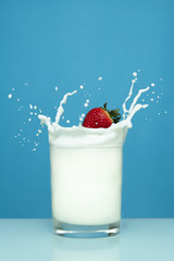 Milk splash with strawberry in glass on blue background.png