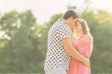 husband gently hugs his pregnant wife in a pink dress. couple in