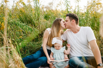 Happy young family in park on vacation together. The father, mother, baby girl sits on blanket,...