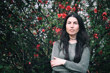 Lovely young  girl with big brown eyes and long dark hair  smiles and rejoices near the green tree in the garden. Dark background.