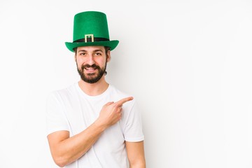 Young caucasian man wearing a saint patricks hat isolated smiling and pointing aside, showing something at blank space.