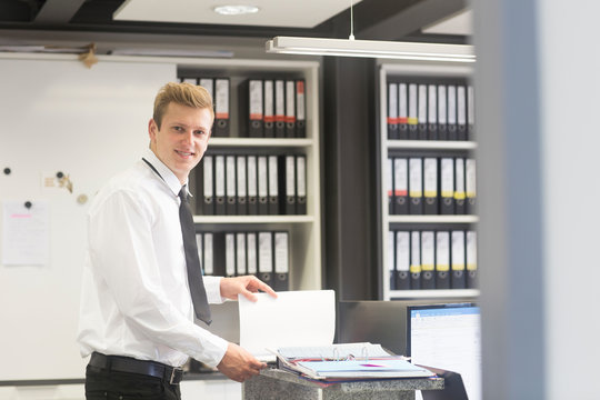 Smiling Salesman standing in a shop's office looking at a brochure, Germany