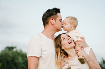 The daughter hugging parents on nature. Mom, dad and girl toddler,  walk in the grass. Happy young family spending time together, outside, on vacation, outdoors. The concept of family holiday.